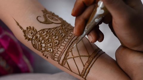 Master is performing mehndi beauty  treatments in Indian wedding ceremony. Man is decorating hands of client girl by temporary henna tattoos