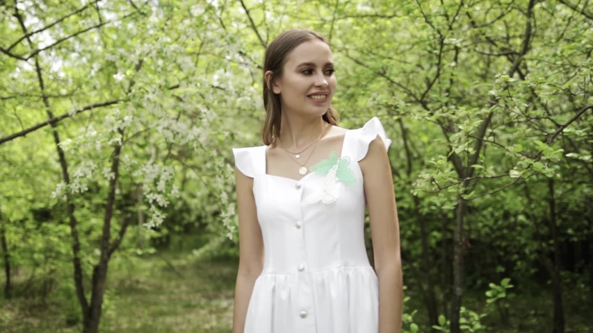 Cute girl posing in a white dress in front of a blooming garden, blooming Apple trees, summer, spring, beautiful nature