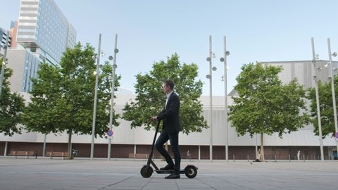 Young businessman riding an electric scooter for a business meeting in the office, office buildings, business man, sunset, electric transport, ecological transport, 4k, e-skateboard