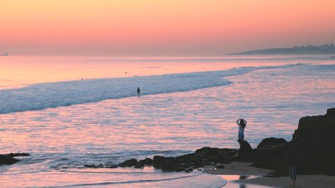Incredible beautiful sunset sky reflections, atlantic ocean waves at Carcavelos beach, Orange teal blue tones, Man walking in low tide water waves.