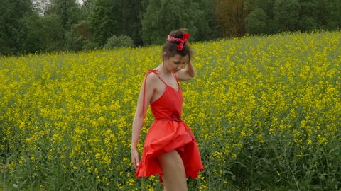 young sexy woman in red twirl on yellow rape field