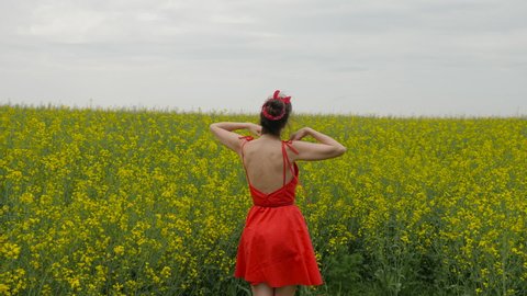 young sexy woman in red twirl on yellow rape field