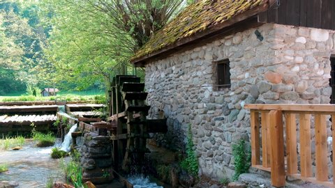 A rustic waterwheel turning in a small stream, attached to an old stone building.
