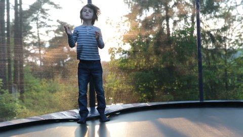 Sweet preteen boy jumping on trampoline making somersaults in the air. Child levitating. Happy child jumping on sunset