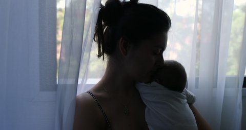 Silhouette of mother holding newborn baby son in her arms next to window