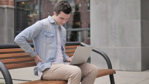 Young Man with Back Pain Working on Laptop Outdoor