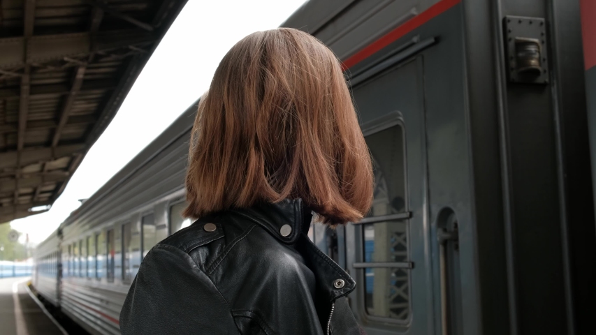 Attractive red-haired young woman with short haircut, wearing glasses and black leather jacket is standing at beautiful historic Vitebsk railway station in St. Petersburg and waiting for train.