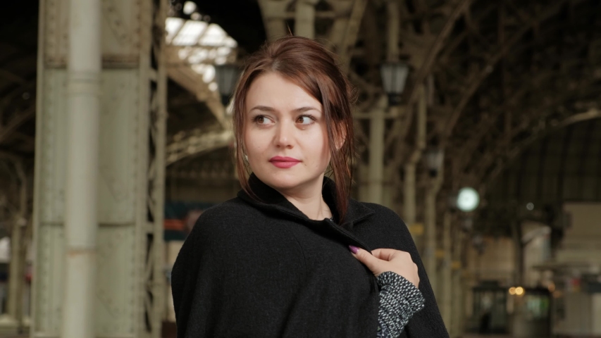 Attractive middle-aged brunette woman in a black coat at the railway station. Waiting for the train.