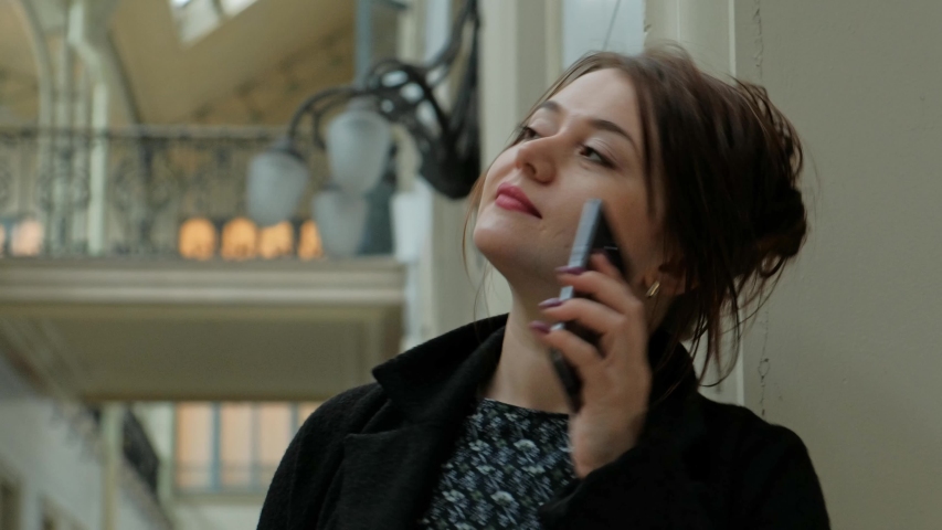 Attractive middle-aged brunette woman in a black coat speaks by phone in the historic station building.