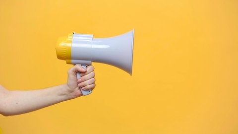Close up female hold in hand bullhorn public address megaphone isolated on yellow background. Hot news, announce discounts sale, hurry up, communication concept. Copy space. Advertising area, mock up.