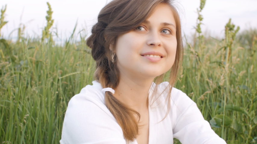 young beautiful rural girl sitting in a field on the grass and smiling, women emotions and springtime, concept of human beauty and nature, relaxation, harmony