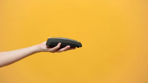 Close up cropped of female hold in hand wireless modern bank payment terminal to process acquire credit card payments black card isolated on yellow background. Copy space mock up advertising, man pay