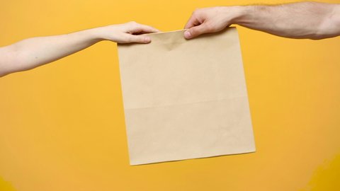 Close up female hold in hand brown clear empty blank craft paper bag for give takeaway isolated on yellow background. Packaging template mock up. Delivery service concept. Copy space. Advertising area