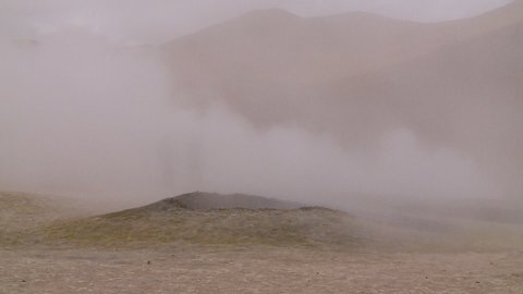 Wide low-angle still shot of two men covered by white thick geyser vapours at Sol de Ma ana, Atacama, Bolivia