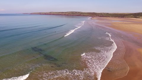 Aerial shot looking across the sandy beach at Freshwater west in Wales, with small waves and sunny skies, while panning right.