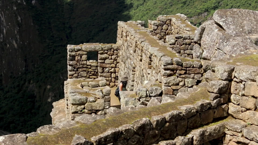 Medium high angle still shot of ancient stone walls ruins facing the Sacred Valley, and a female tourist visiting the site, Machu Picchu, Peru