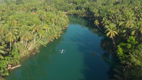 Aerial drone bird's eye view pull-down shot of a boat across a river surrounded by a tropical rain forest in Loboc Philippines