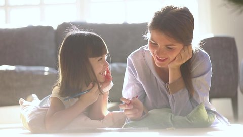 Caring mom babysitter teaching coloring drawing with pencils talking to little girl at home in lit with sunlight room, happy mother and child daughter play together enjoy creative kid parent activity
