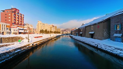 Daytime beauty after a winter snowfall of the Otaru Canal in Hokkaido, Japan, a popular skiing destination. Traffic passing on a street and wind blowing across the surface of calm water.