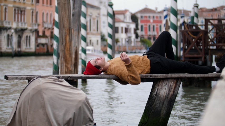 A man lying on the bench above the water and smokes