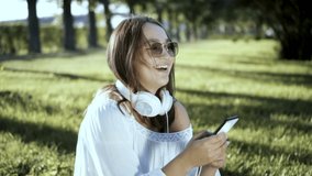 Portrait of laughing girl using her mobile phone wearing colorful hipster sunglasses and headphones Slow motion.