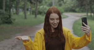 Young attractive redhead girl talking to a friend using a smartphone while being in the forest in the rain. in slow motion. Shot on Canon 1DX mark2 4K camera