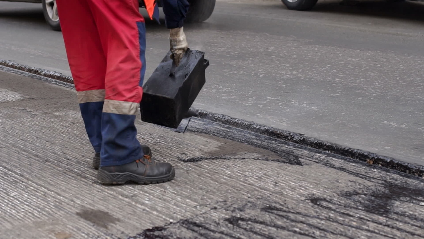 Road repair. Work details, workers pour resin road surface to cover the asphalt. Men in specialized clothing repair asphalt in the city. Preparation of asphalt pavement for laying new asphalt. | Shutterstock HD Video #1030521239