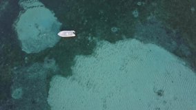 Drone shot glides over still boat on clear blue sea