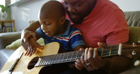 Front view of African american father teaching his son how to play guitar at home. Social distancing and self isolation in quarantine lockdown for Coronavirus Covid19