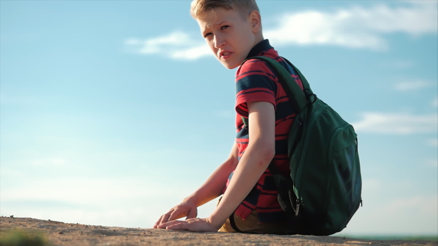 Teenager in a red shirt with a backpack behind him, at sunset, sitting on a high hill, enjoying nature, freedom, begins to speak turns to the camera and says.