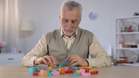 Positive old man playing with wooden cubes, cognitive training in Alzheimer