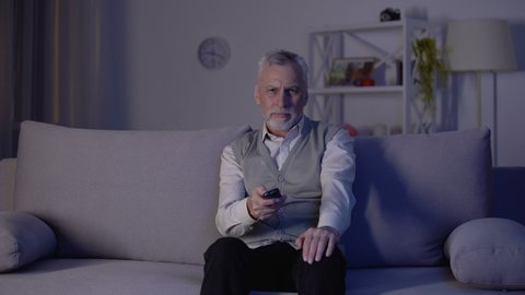 Old man switching channels with remote control, bored and annoyed with ads