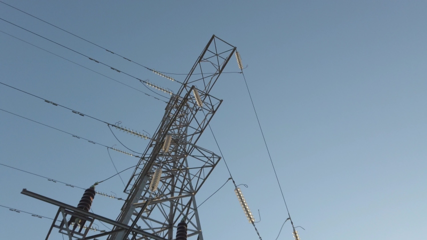Upward perspective view of pylon structure & high voltage lines against blue sunrise sky. Royalty-Free Stock Footage #1030543142