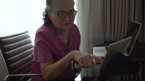 Asian senior woman using digital tablet and laptop in living room, learning and study concept