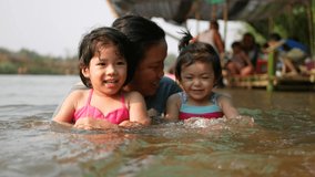Two little Asian baby girls, sisters, enjoys playing water in a river with her auntie - playing outdoor and engaging with nature provides positive impact on baby's health and development