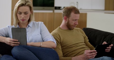 Attractive couple surf on tablets whist ignoring each other, showing what is wrong with modern technology, in slow motion