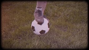 The camera moves around the boy. Brown shoes. Worn sneakers, boots. Ball on green grass. Family video. Archived video. Old film. Famous footballer in childhood. Children's sport. Family holiday.