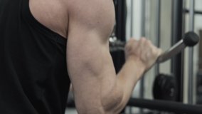 Strong muscular guy performing tricep pull downs during gym workout. Focused man training triceps muscles pulling cable machine in gym