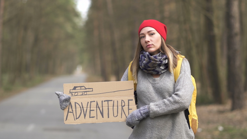 Young pretty hitchhiking woman stand on road with poster Adventure  .Travel emotion