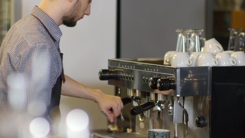 Tilting waist-up shot of tattooed Caucasian male barista making double espresso in coffee shop, flushing group head with water, inserting portafilter, putting ceramic cup underneath and watching 스톡 비디오