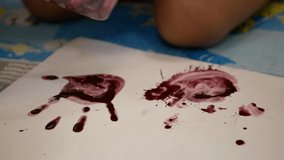 Close up of a little baby girl's colored hand pressing down on white paper, with help from her mother - baby handprint / fingerprint painting