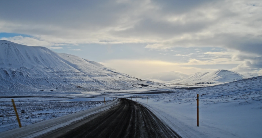 Driving along a deserted, snow covered, mountain road in Iceland under the midnight sun.