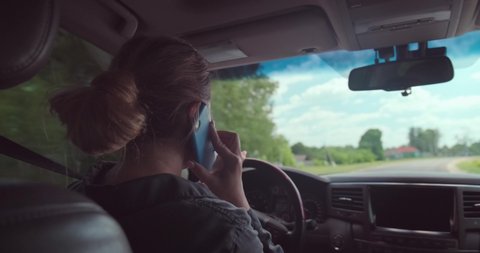 Woman drives the car. Happy woman in the car speaking on the phone. Beautiful adult smiling woman is driving the car. White adult girl talks by mobile while driving an automobile. Real time. Inside.