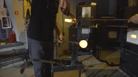 Glassblower taking the rod with liquid glass out of glowing hot oven in his workshop .