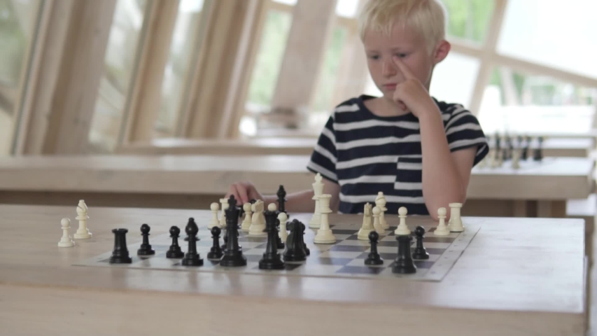 The boy plays chess. The child sits in a spacious bright chess club and waits for the opponent's turn. | Shutterstock HD Video #1030593107