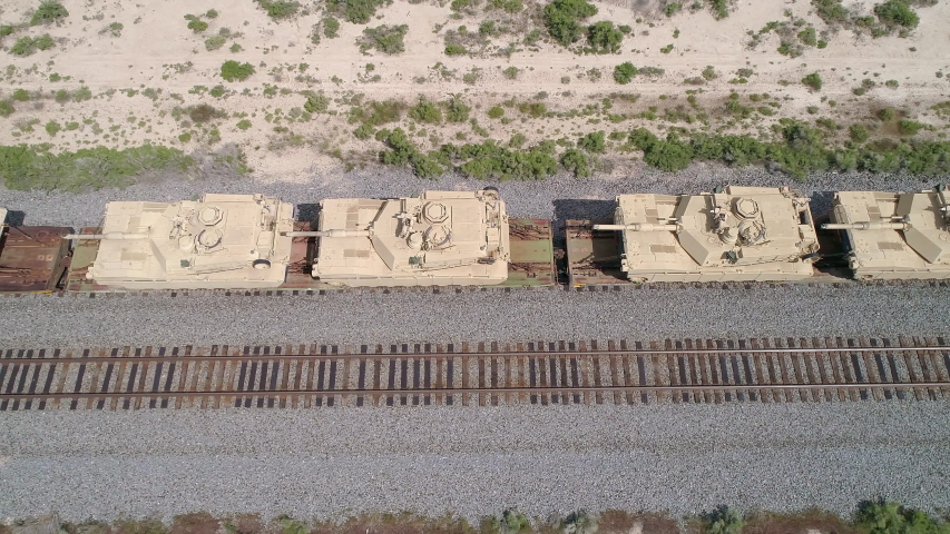 Aerial view looking town at tanks loaded on a train looking down at the tracks in the desert.