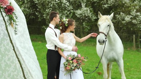 Bride with groom and white horse to side of them with wedding teepee and table fully decorated.