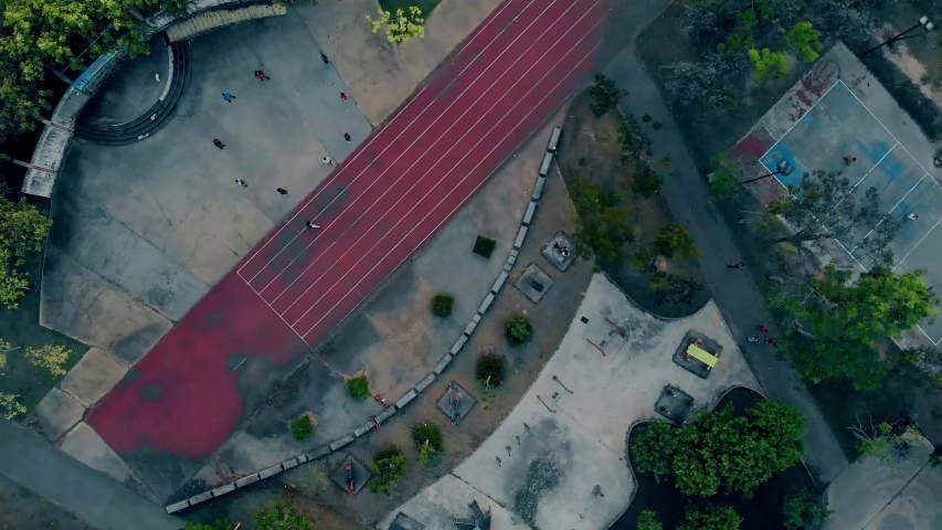 abandoned old blue playground basketball court and long red running track between thick green forest bird eye view
