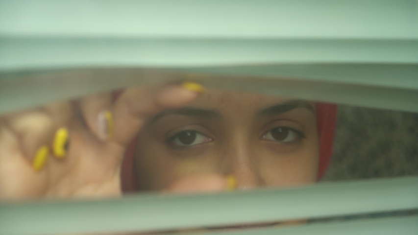 funny caucasian woman with red towel on head pry and looking at camera through the jalousie in the hotel. Close up