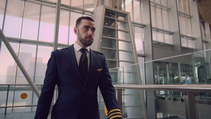 Stylish handsome bearded pilot puts on his pilot cap, corrects the uniform and confidently leaves the airport. Day off, weekend, profession concept. Male portrait